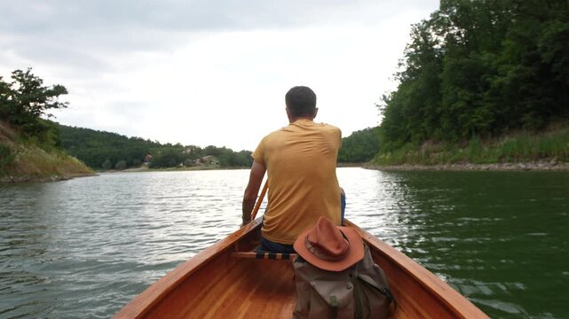 Man paddling wooden canoe on peaceful lake
