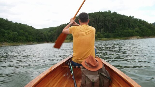 Rear view of a man paddling a wooden canoe across a calm lake