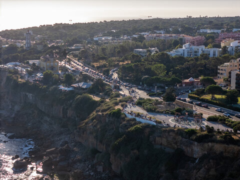 Cascais, Portugal - 12 August 2026: Aerial view of Guia lighthouse and coastal cliffs, with a busy road, lush greenery, and the Atlantic Ocean under soft afternoon light.