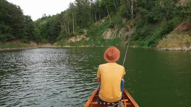 Rear view of a man fishing from a wooden canoe on a forest lake