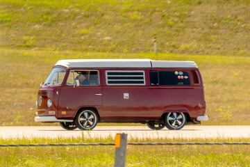 Fototapeta premium Calgary, Alberta, Canada. August 15, 2026. Side view of vintage red Volkswagen Westfalia camper van driving along highway on sunny day.