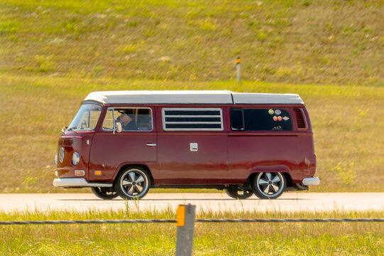 Calgary, Alberta, Canada. August 15, 2026. Side view of vintage red Volkswagen Westfalia camper van driving along highway on sunny day.