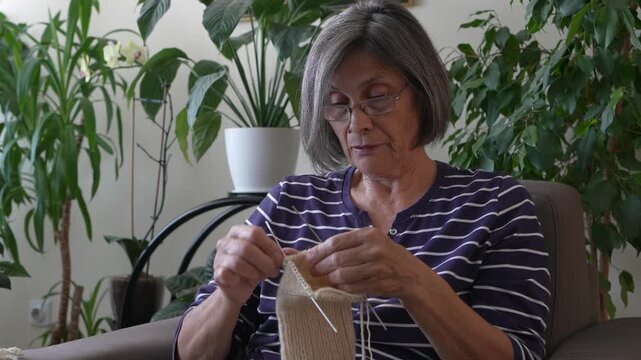 Elderly woman knitting a wool garment with knitting needles  at home