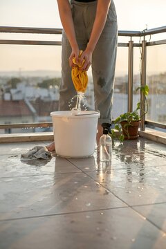 Person wringing cleaning cloth on balcony at sunset. 