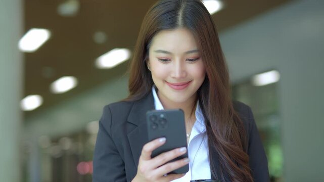 Close-up of Asian businesswoman using mobile phone, texting and cheating on her smartphone while outside office.