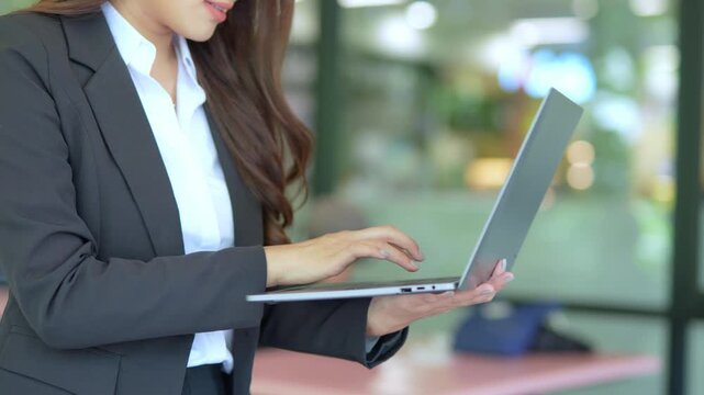 Asian businesswoman working at desk using laptop and notebook talking to client or office building, slow motion footage