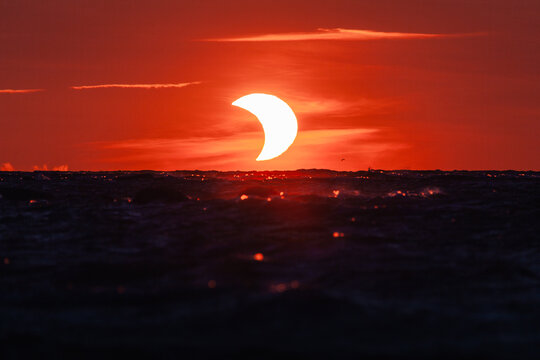 View of a partial solar eclipse over the dark sea at sunset with a vibrant red sky in Merikula, Harju maakond, Estonia.