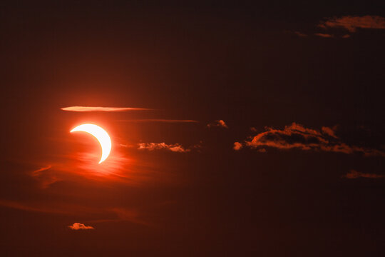 View of a partial solar eclipse with the sun partially obscured by the moon, set against a dark, dramatic sky with glowing orange clouds in Merikula, Harju maakond, Estonia.