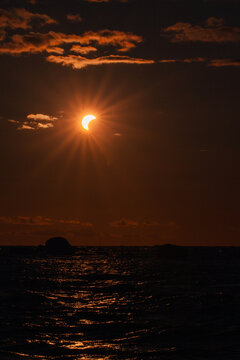 View of a partial solar eclipse over the dark sea with dramatic sun rays and clouds at sunset in Merikula, Harju maakond, Estonia.