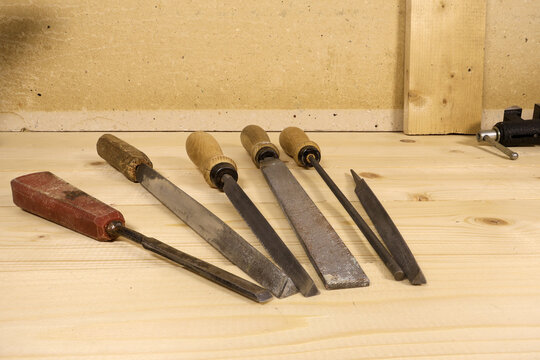 Set of vintage woodworking chisels with brass ferrules and worn blades rests on light wooden workbench