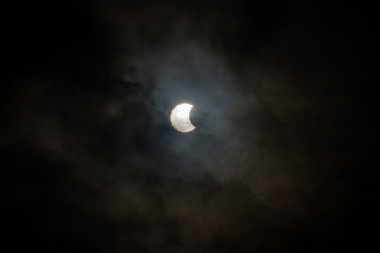 Iceland - 12 August 2026: View of a partial solar eclipse partially obscured by dark, moody clouds in the night sky over the Westfjords Region.