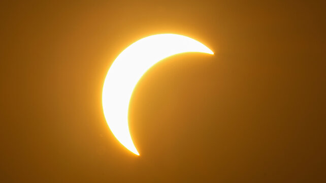 Geneva, Switzerland - 12 August 2026: View of a partial solar eclipse with the moon partially obscuring the sun against a hazy golden sky.