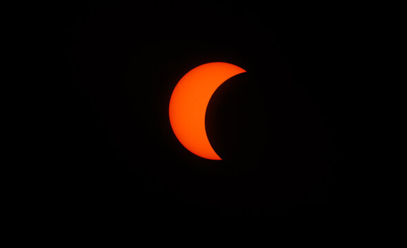 Spain - 12 August 2026: View of a partial solar eclipse with the moon obscuring a portion of the sun against a dark background.