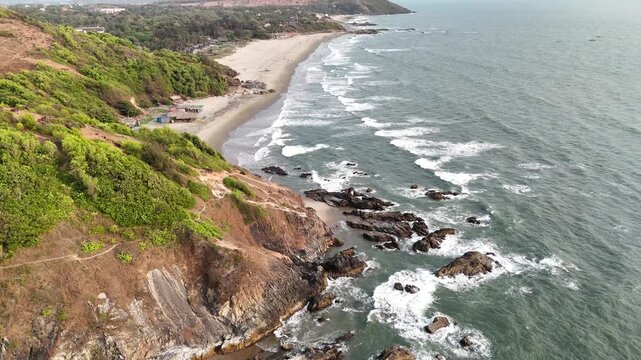 Complete aerial view of Vagator Beach from end to end, Goa, India. Full coastal landscape showing the long sandy shore, dramatic cliffs, and ocean waves.