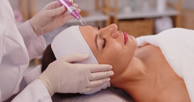 Portrait of happy beautiful woman lying on couch in cosmetology cabinet and receiving apparatus facial treatment procedure. Cosmetologist working in beauty spa salon. Skin care concept. 4k video.