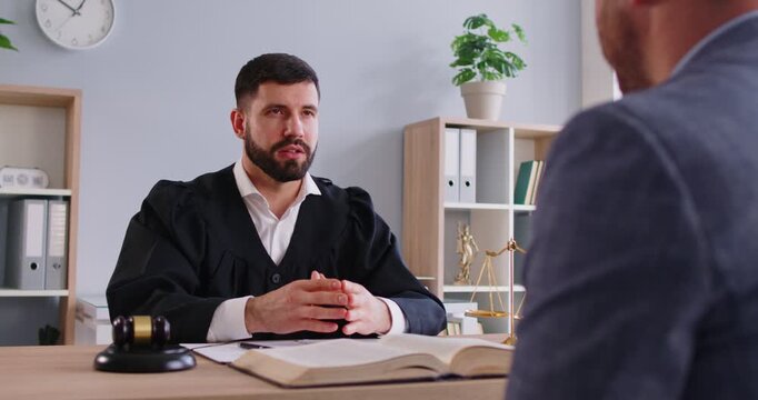 Unknown man talking to professional lawyer, sitting at office desk, getting law consultation. Judge having talk with client, giving statement, helping with legal documentation. Law guidance