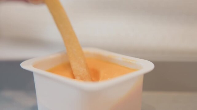 Low-angle close view shows spoon mixing thick yogurt in open cup, with rippling surface, rising column, and trailing peak that suggest fresh dairy texture for snack, recipe, and packaging use