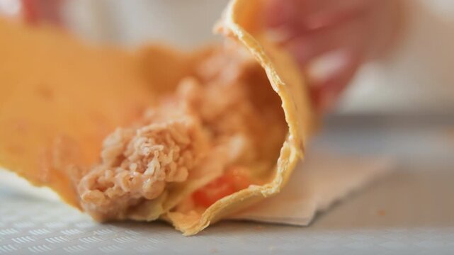 Macro view of torn crepe pulled open to reveal creamy shredded filling with small vegetable pieces, filling spilling onto napkin while blurred fingers hold subject in warm soft light