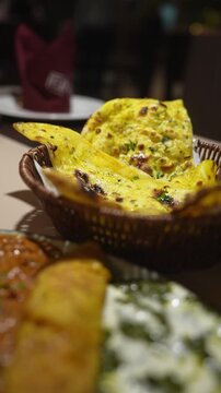 Vertical video close up rack focus from yellow butter garlic naan basket to stuffed roll served with creamy spinach and rich tomato curry gravies on dining table