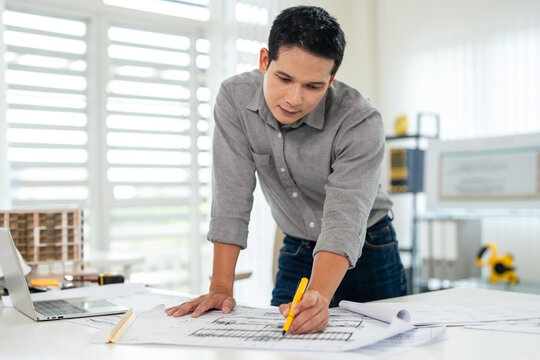 Young asian civil engineer studying a blueprint floor plan and  working with documents, drawings and building models.