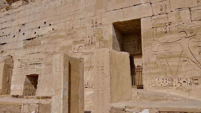 Medinet Habu temple ruins with column bases altar and walls against desert mountain backdrop in Luxor Egypt, ancient pharaonic archaeological site with clear blue sky.