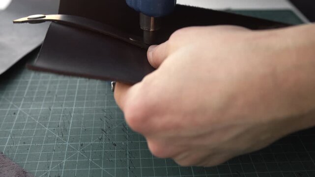 Craftsman installing a metal rivet on a dark brown leather strap using a manual press machine in a workshop