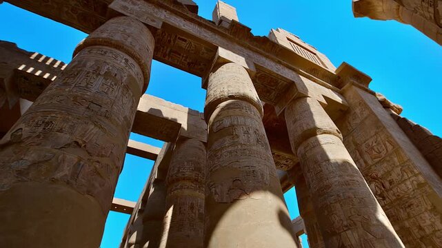 Karnak Temple in Luxor, Egypt. Massive hieroglyphic columns in Great Hypostyle Hall, Karnak Temple Luxor Egypt. Upward view of ancient carved pillars against blue sky.