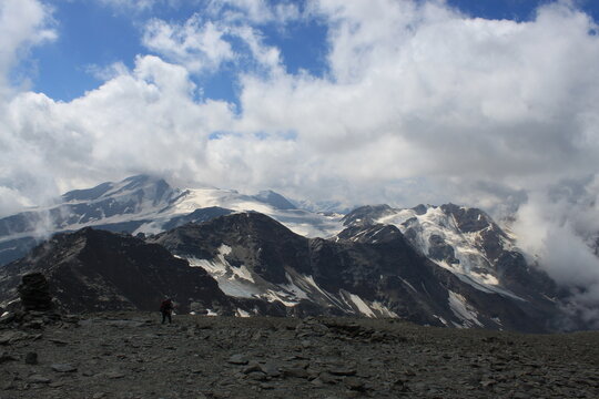 Hiker crossing rocky alpine plateau beneath glaciers near Solda