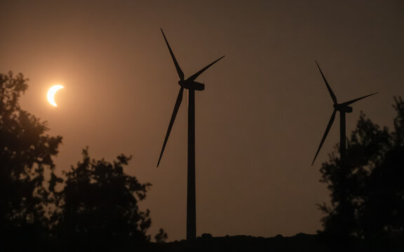 Villaferruena, Castile and Leon, Spain - 12 August 2026: View of a solar eclipse with the moon partially obscuring the sun behind wind turbines at a wind farm.