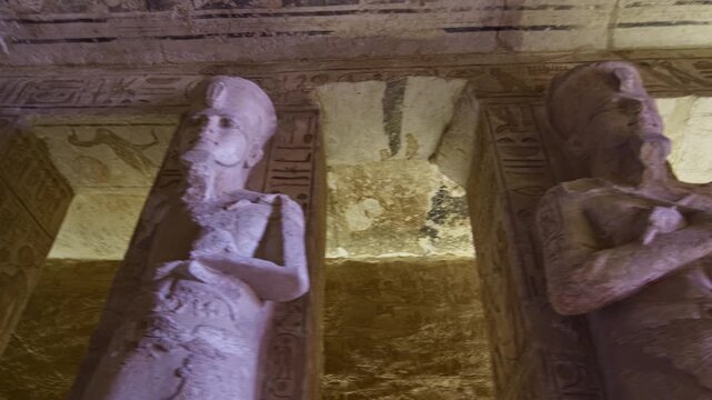 Symmetrical row of colossal Ramesses II osiride pillars lining both sides of main hall at Abu Simbel temple, Egypt, faded painted ceiling with vultures above.