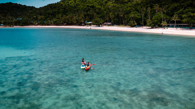Group of tourist are enjoy on water sport paddle sup-board with kayaking along at the edge of the sea beach under crystal clear of water in the island of summer trip