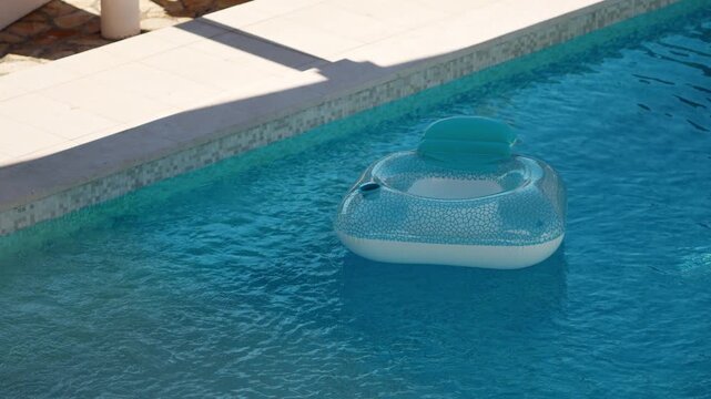Inflatable pool floats in private villa pool during the summer. Sunlight reflects off surface of the water. Light plays on blue tiled bottom underwater. Gentle breeze. Pula, Croatia - August 15, 2026