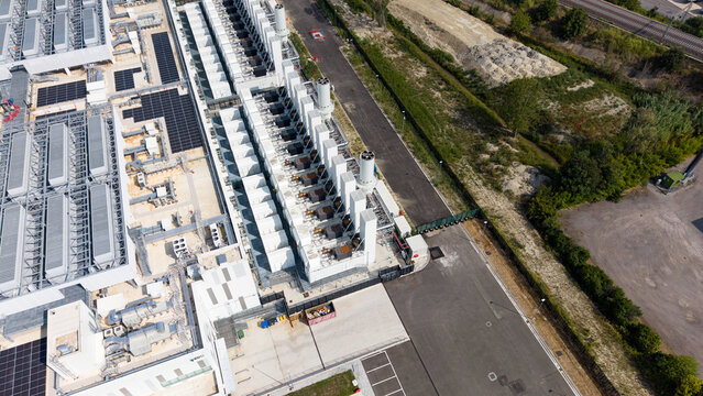 Aerial view of a modern hyperscale data center featuring rows of cooling units, server infrastructure, and solar panels, located in an industrial area in Melegnano, Lombardy, Italy.