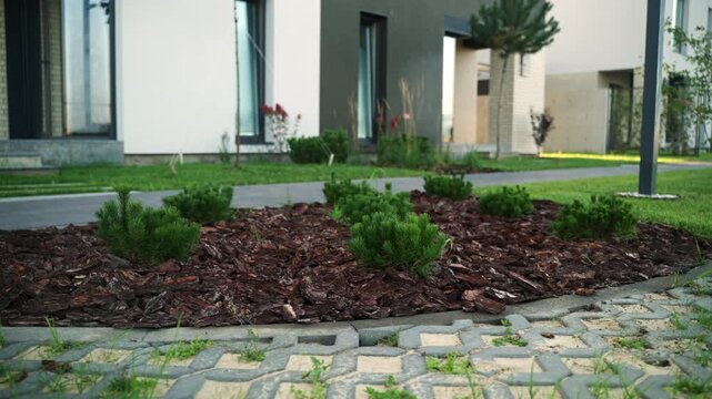 Landscaped grounds of a contemporary residential complex featuring decorative mulch with small bushes, green lawns, and permeable grass pavers for an eco-friendly parking area
