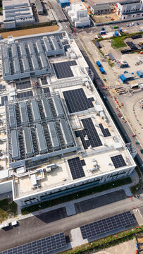 Aerial view of a modern hyperscale data center featuring extensive rooftop solar panel arrays, cooling units, and surrounding industrial infrastructure in Melegnano, Lombardy, Italy.