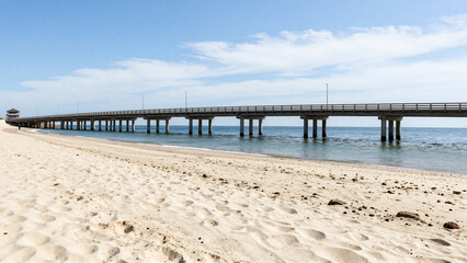 Fototapeta premium Long Concrete Bridge Over Sandy Beach and Blue Ocean