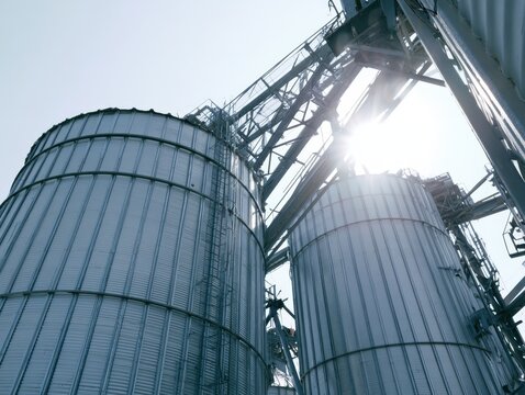 Metal grain silos elevator tanks storage facility at agricultural factory under blue sky. Industrial agribusiness infrastructure, food production logistics and farming distribution warehouse solution.