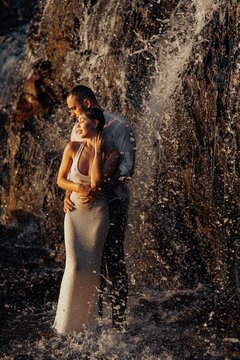 Romantic couple standing under waterfall spray in sunset light