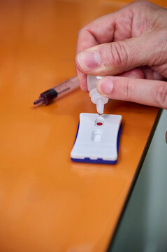 A veterinarian's hands pouring a drop of blood onto a rapid veterinary test kit on an orange table.