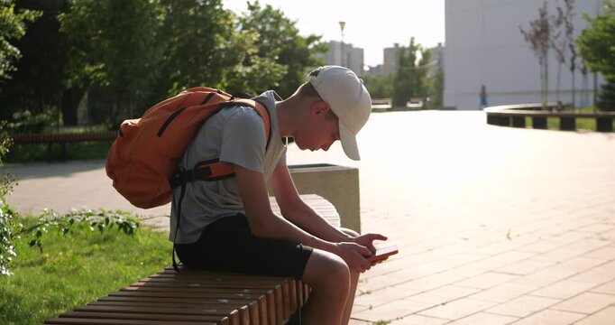 Young boy hunches over smartphone while sitting on city bench. Poor posture highlights common effects of prolonged screen time, sedentary habits and excessive smartphone use.