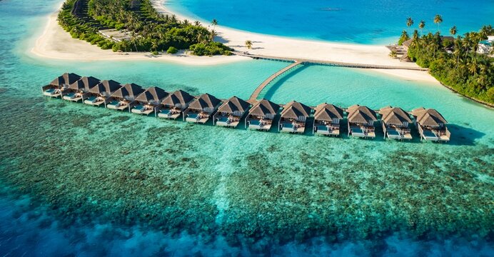 Amazing aerial Maldives water villas, turquoise ocean lagoon, coral reef, palm trees sand tropical island. Stunning summer travel landscape paradise. Luxury drone honeymoon background vacation view