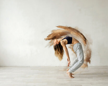 Woman performing a dynamic dance move with airborne dust against a white background