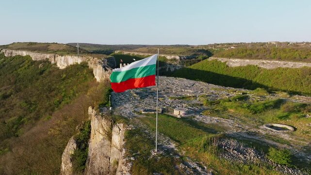 Waving Bulgarian national flag on pole Ovech Fortress plateau cliff edge aerial drone view medieval stronghold ruins Provadia landscape travel destination Bulgaria