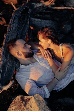 Romantic couple lying together leaning on dry log and looking at each other in sunset light