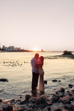 Full length passionate couple embracing in water about to kiss at sunset, young man and woman on river shore