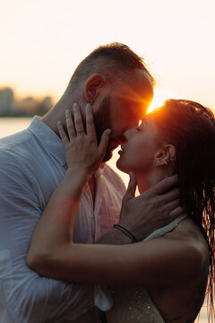 Passionate couple kissing at sunset, romantic lovers touching faces in golden sunlight flare