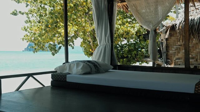 Outdoor mattress with white pillows resting on wooden platform, tropical beach bungalow overlooking turquoise ocean and limestone cliffs, luxury vacation background, travel marketing