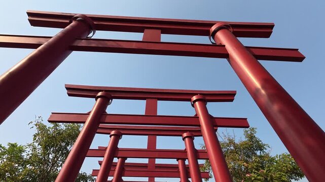 Gresik, Indonesia - August 13, 2026: Low angle moving shot of red Japanese Torii gates replica against a clear blue sky at a local tourist park.