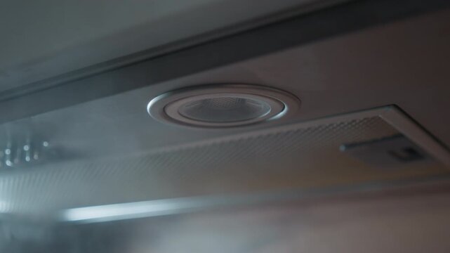 Low-angle close-up shows recessed circular ceiling vent beside smooth panel, with visible steam or mist rising past fixture, soft diffuse light, warm spill, and subtle indoor atmosphere