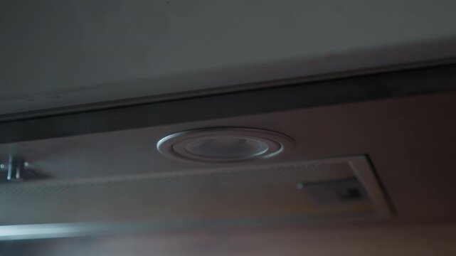 Low-angle view of ceiling vent beside recessed light, with bright warm glow, rising steam, gentle airflow, soft diffusion, reflective metal surface, and humid indoor atmosphere creating subtle motion